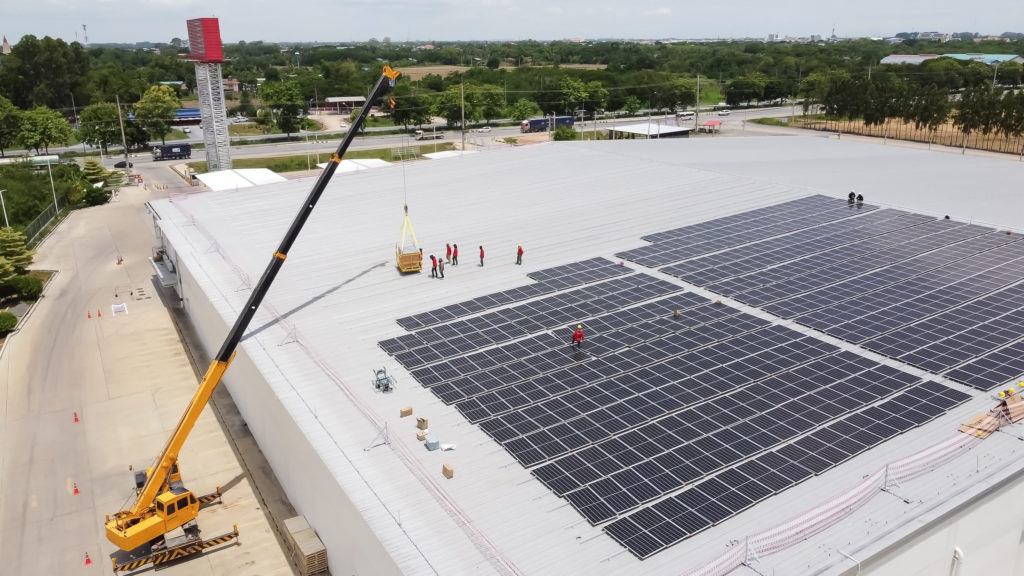 Žeriav inštaluje solárne panely na budovu fabriky.